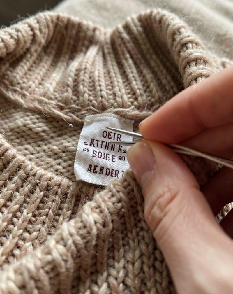 A bolt of wool fabric with a paper tag bearing a skein-like symbol, tailor's chalk and shears beside it